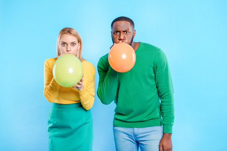 Cheerful man and woman inflating colorful balloons