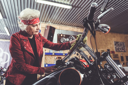 Thoughtful pensioner polishing bike in mechanic shopの写真素材