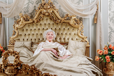 Confident old woman lying on expensive bedの写真素材