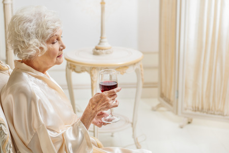 Lonely mature woman holding glass of alcoholic drinkの写真素材