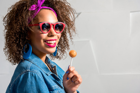 Cheerful african female with curly hair and with colorful accessories keeping candy and laughing. Copy spaceの写真素材