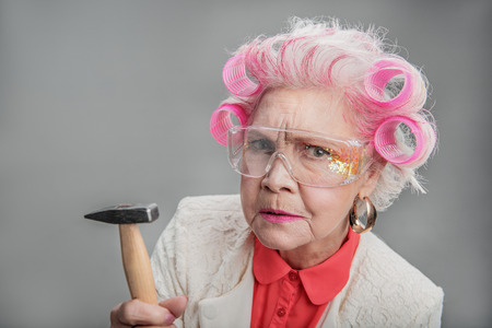 Whom are you calling old. Portrait of Stylish elderly woman in curlers holding hammer while posing at camera. isolated backgroundの写真素材