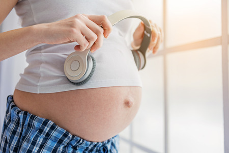 Expectant mother enjoying music in bedroomの写真素材