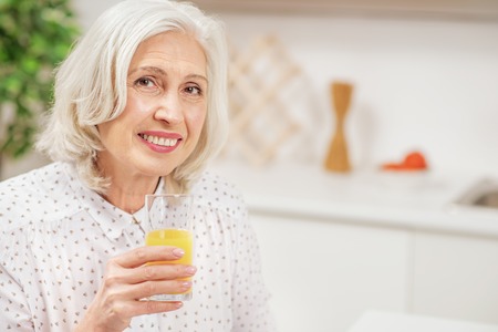 Happy senior woman drinking juice in kitchenの写真素材