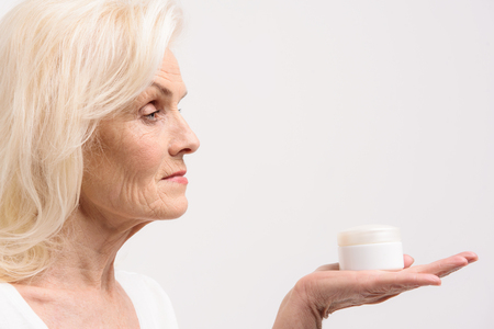 Interested woman keeping white jar with moisturizerの写真素材