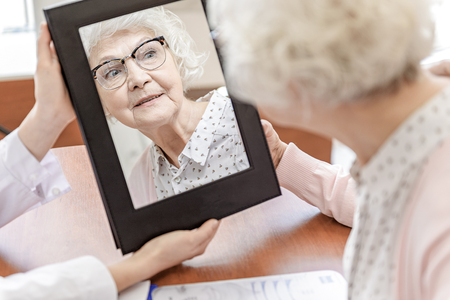 Interested old woman glancing in mirrorの写真素材