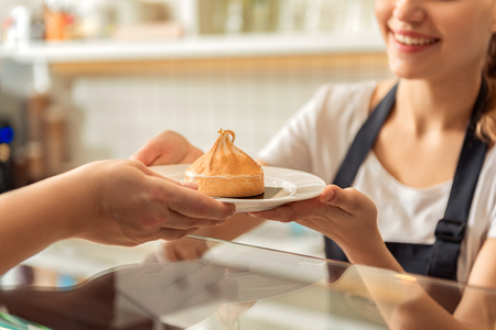 Cheerful saleswoman handing pastry to clientの写真素材