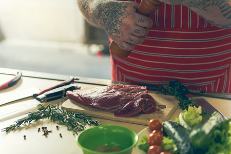 Fat man adding spices to fresh pork meatの写真素材