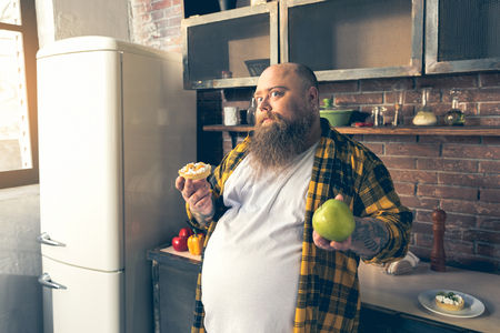 Thick guy making choice between healthy and unhealthy foodの写真素材