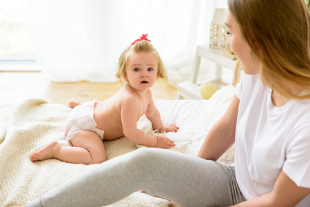 Cute baby sitting near mother on beddingの写真素材