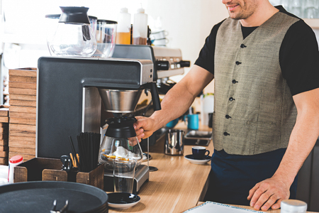 Happy bristled barista preparing mug of appetizing coffee with special equipment in candy storeの写真素材