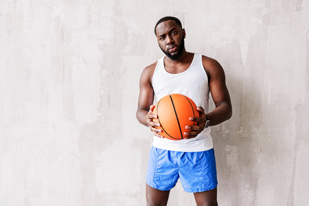 Deep looking bearded athlete standing by wall with basket-ball in armsの写真素材
