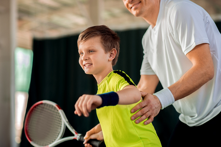 Happy man teaching his son on tennis courtの写真素材