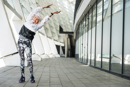 Joyful elderly lady warming up by modern city buildingの写真素材