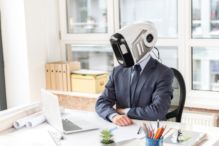 Pleasant businessman with head of robot looking at screenの写真素材