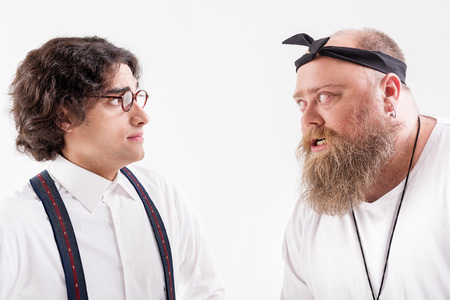 Irritated male hipster talking to frightened smart guyの写真素材