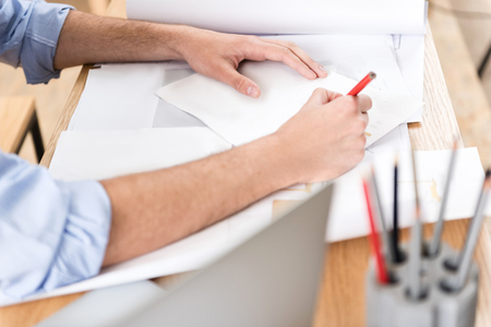 Youthful man making picture of manufacture on paper at workplace