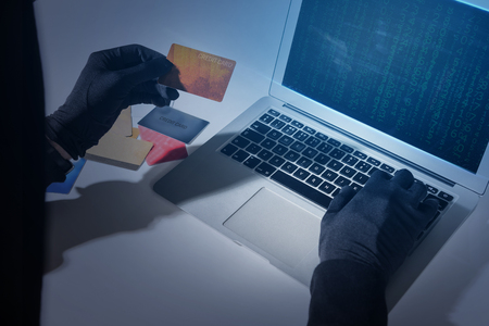 Electronic banking security concept. Close up top view of hands of hacker wearing gloves. Burglar is stealing money from credit card using laptop while sitting at deskの写真素材