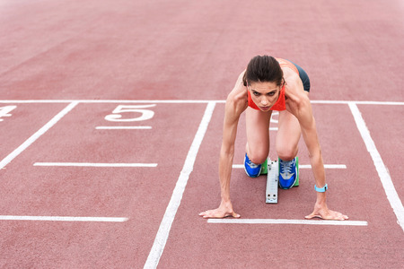 Confident girl posing in blocks to start runningの写真素材