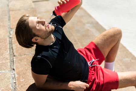 Exhausted sportsman with beard refreshing after training outdoorの写真素材