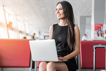 Pleasant stylish girl is sitting on red bench with computerの写真素材
