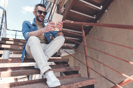 Joyful adult bearded man is checking emails on electronic deviceの写真素材