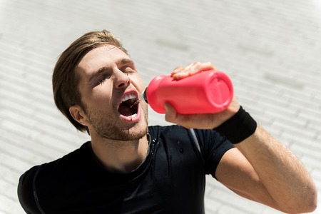 Worn-out young athlete satisfying thirst outsideの写真素材