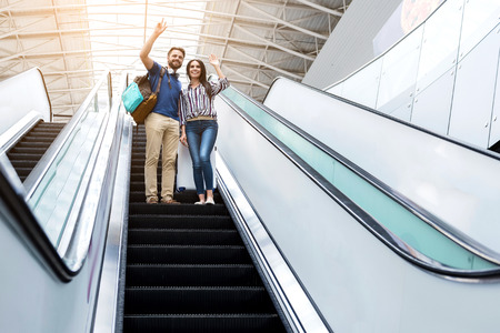 Joyful couple is standing on escalator and expressing gladnessの写真素材