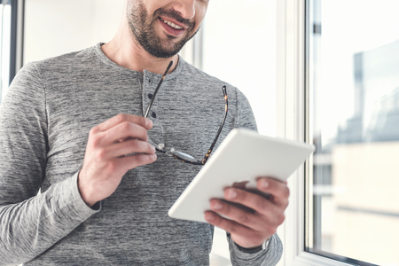 Cheerful adult businessman is reading emails using modern gadgetの写真素材