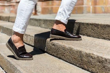 Close up of legs of young man in white jeans stepping up city ladder outdoor. He is wearing leather...