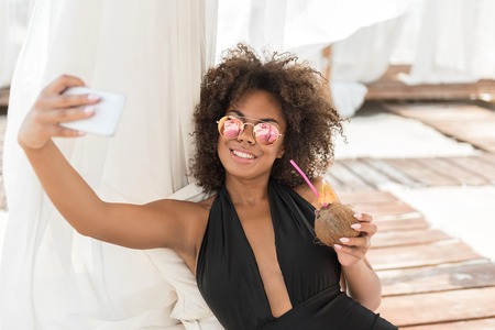Happy youthful african girl relaxing with gadget on beachの写真素材