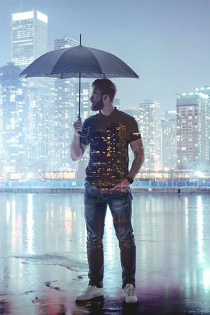 Pensive guy posing on rainy cityscape backgroundの写真素材