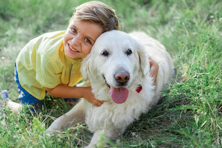 My best friend. Portrait of happy boy hugging his dog and smiling. He is looking at camera with happiness while kneeling on grassの写真素材