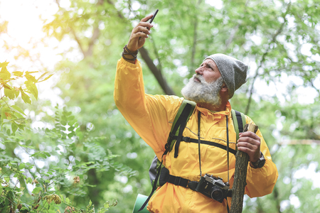 Pensive senior male tourist using his mobile phone in forestの写真素材