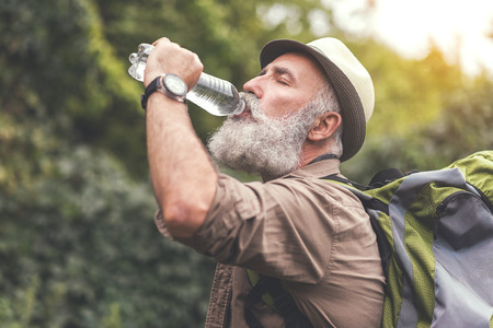 Senior male hiker is very thirsty and drinking waterの写真素材