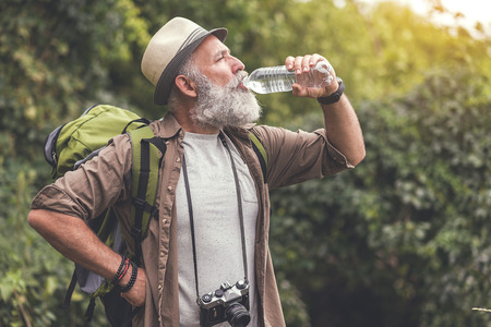 Tired old man drinking water from bottle in woodlandの写真素材