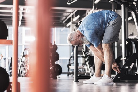 Pleasant old male is having workout in modern athletic club
