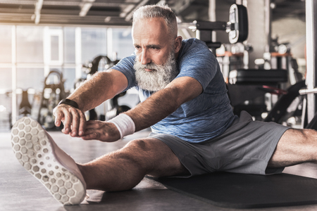 Serious old bearded man is enjoying exercises in fitness centerの写真素材