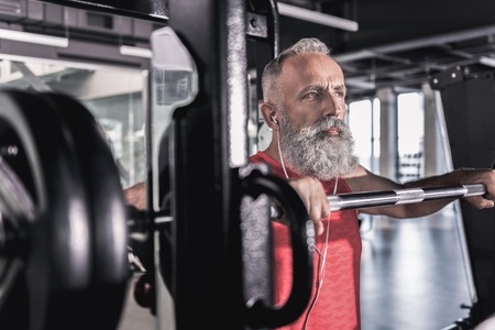 Pensive serious male with beard enjoying workout in athletic centerの写真素材