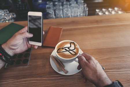Close up male pensioner arm keeping mug of appetizing cappuccino with image of plane on it while...