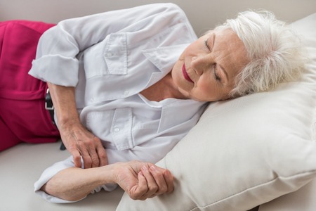 Need to rest. Stylish elegant aged lady is dozing on white couch at her homeの写真素材