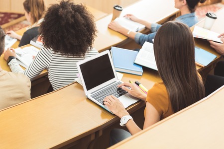 Top view of students sitting at desks in lecture hall. Brunette girl is typing on laptopの写真素材