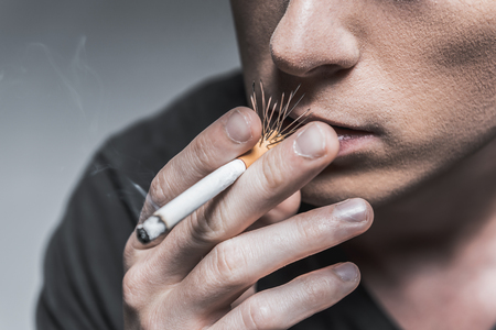 Dangerous smoking. Close up of face of young man smoking cigarette. Focus on needles in filterの写真素材