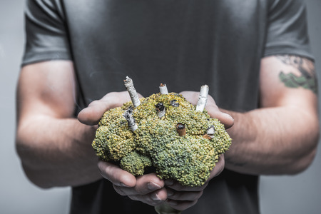 Close up focus on yellowed broccoli with cigarettes inside in male hands. Lungs illness conceptの写真素材