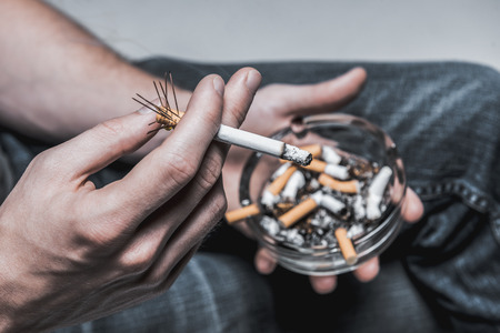 Top view close up focus on human arm holding harmful cigarette while smoking. Man is carrying...