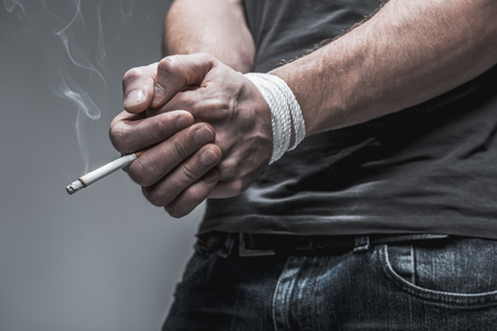 I cannot quit smoking. Close up of tied up arms of young man keeping cigarette. Isolatedの写真素材