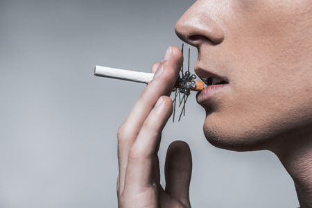 Smoking is dangerous for your health. Close up profile of young man keeping cigarette with needles in his mouth. Isolated and copy spaceの写真素材