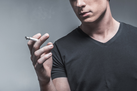 Close up of arm of young guy holding cigarette. He is standing and expressing calmness. Isolatedの写真素材