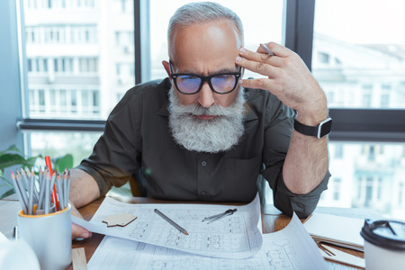 Old bearded engineer is laboring in officeの写真素材