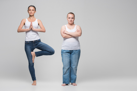 Serene slim girl doing yoga near fat ladyの写真素材